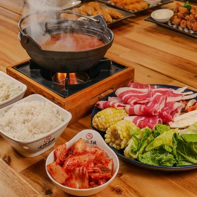 Hot pot meal featuring a pot of savory broth, sliced meats, fresh vegetables and rice.