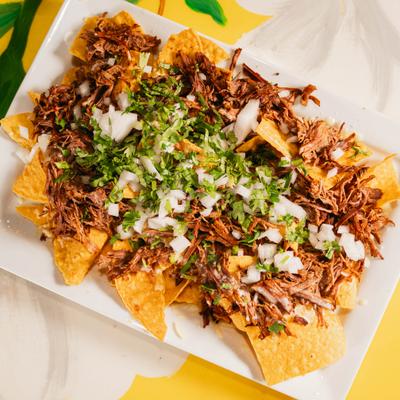 Birria beef nachos topped with shredded meat, diced onions, cilantro, and melted cheese.