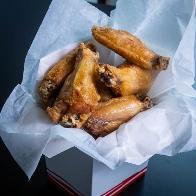 Fried chicken wings in a takeout container with parchment paper.