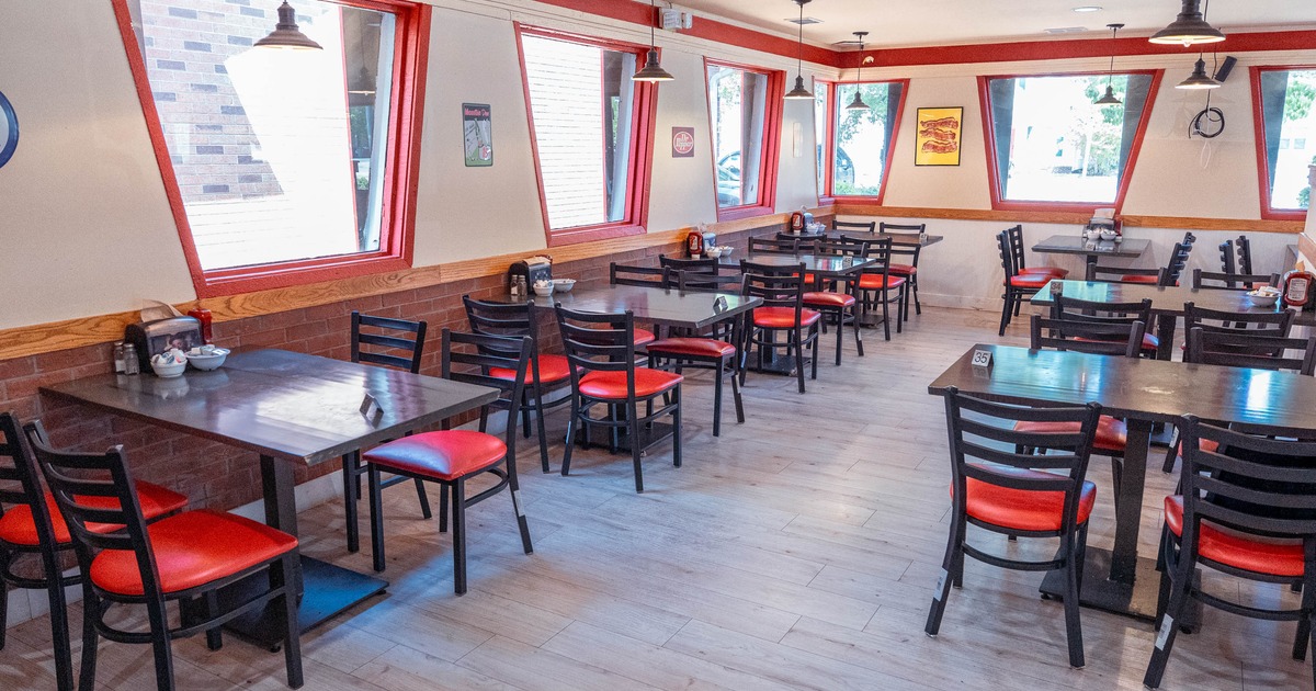 Restaurant dining area with tables and chairs, red accents and slanted windows.