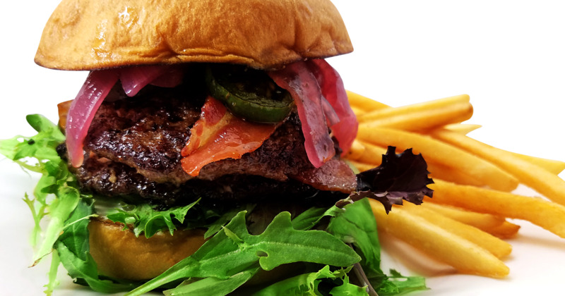 Burger with bacon, lettuce, cream cheese, jalapenos, and a brioche bun.  Fries in the background.