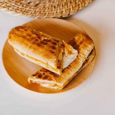 A wooden plate holds Egg N Such breakfast sandwich on a white table with a wooden placement.