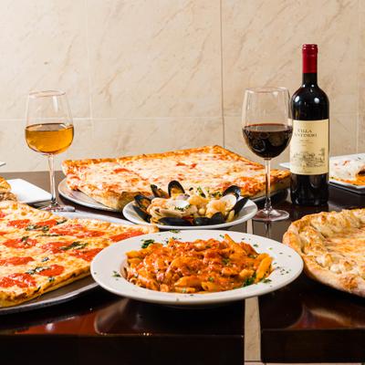 Table with pizzas, pasta and wine glasses.
