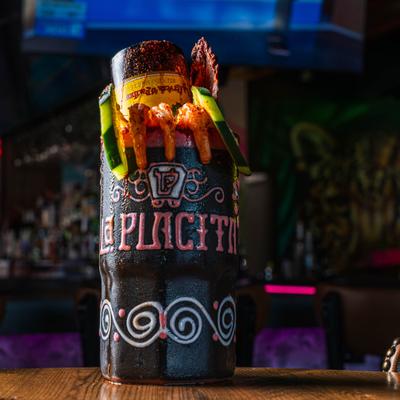 Michelada cocktail with beer bottle inserted into glass and various garnishes.