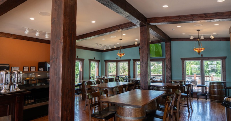 A rustic interior - wooden beams, tables, chairs, large windows and decorative lighting.