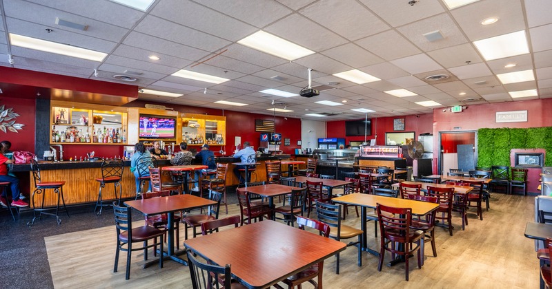 Restaurant interior with tables and a bar, red walls, and a green plant wall