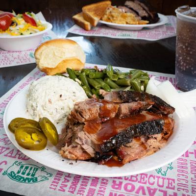 Sliced beef brisket served with various sides, other dishes and a soft drink are in the background.