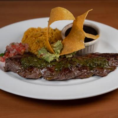 Churrasco steak accompanied by sides of rice, black beans, tortilla chips and guacamole.