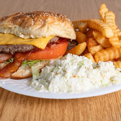 Bacon cheeseburger with crinkle fries and coleslaw on a paper plate.