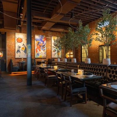 Spacious restaurant with black seating, brick walls, abstract art, and potted trees.