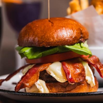 Gourmet burger on a toasted brioche bun with melted brie cheese, bacon, and lettuce.