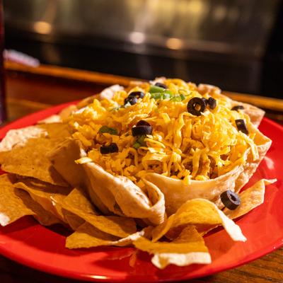Taco salad served in a crisp tortilla bowl with tortilla chips on a red plate.