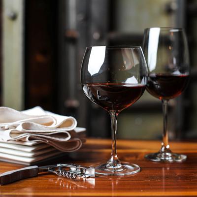 Two glasses of red wine served with a corkscrew and wine cloth.