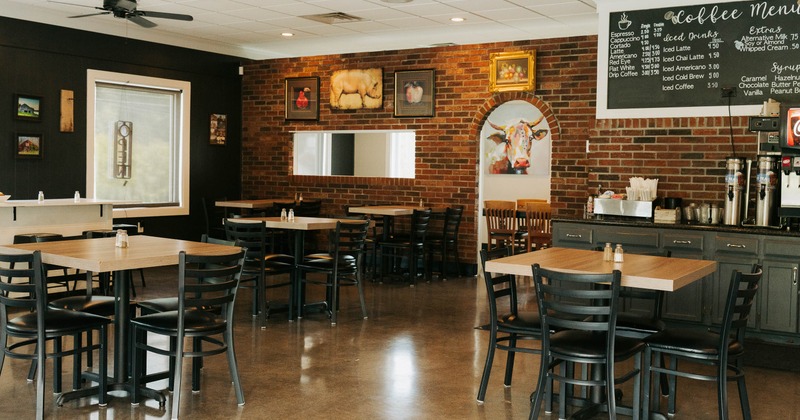 A cozy interior - wooden tables, black chairs, an exposed brick wall, a coffee menu board.