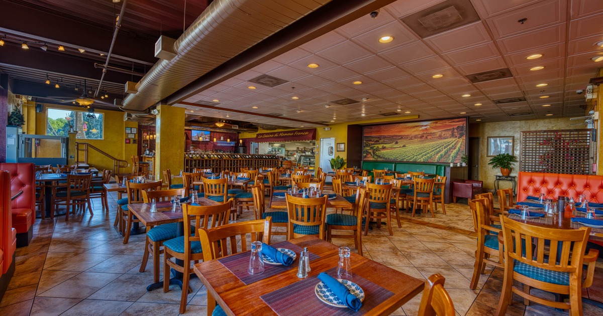 Interior - wooden tables, blue-cushioned chairs, a mural of a vineyard and a bar area.
