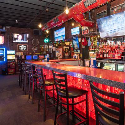 Interior with a long bar with several bar stools and multiple television screens.