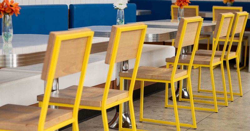 Dining area with yellow chairs, blue benches, and tables with flower vases