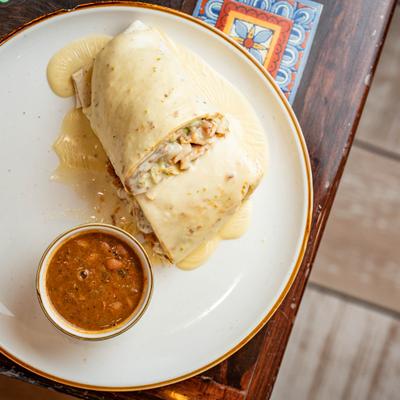 Smothered burrito topped with queso served with a side of beans.