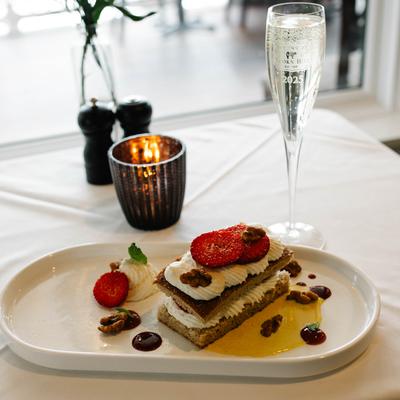 Layered dessert with cream, strawberries, and nuts served with a glass of champagne.