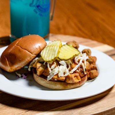 Chicken sandwich on a toasted brioche bun, topped with pickles and coleslaw.