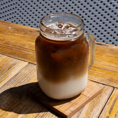 Iced latte in a mason jar on a sunlit outdoor table.