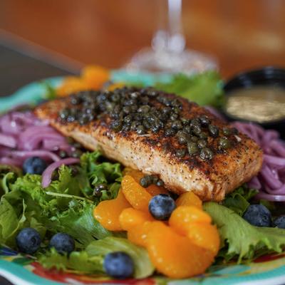 Seared salmon filet topped with capers, served over mixed greens, blueberries, and tangerines.