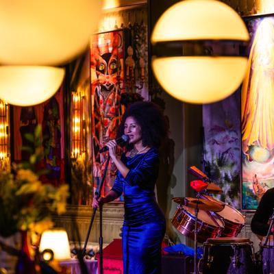 Singer holding the microphone during the live performance, colorful paintings in the background.