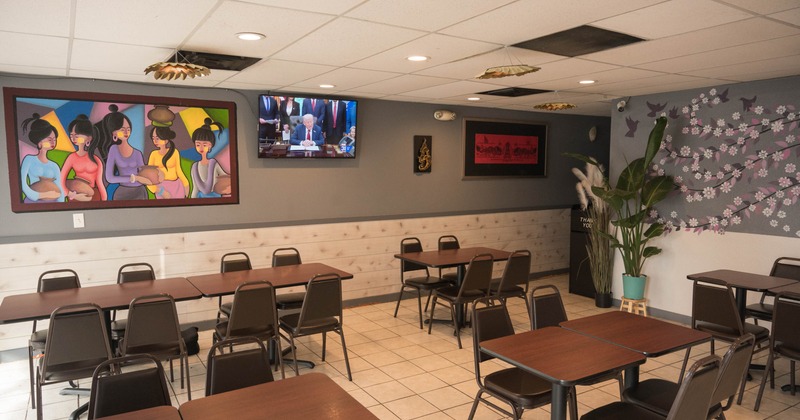 A restaurant interior with wooden tables, colorful artwork, and a TV on a wall