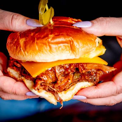 Juicy pulled pork sandwich in hands, close up.