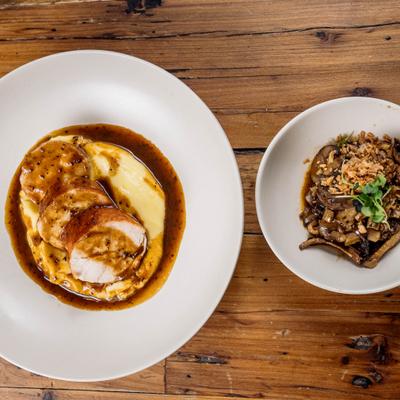 Roasted chicken served over a creamy base, paired with a side dish of sauteed mushrooms.