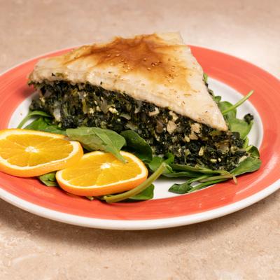 Spinach and cheese pie served on fresh spinach leaves, garnished with orange slices.
