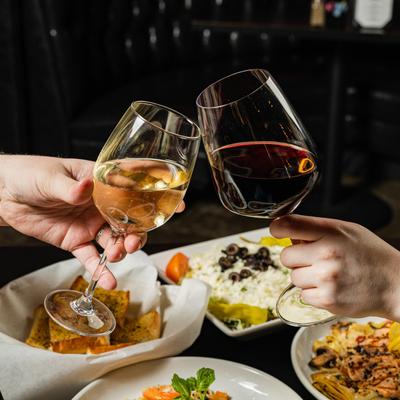 Hands clinking wine glasses over the table with served dishes