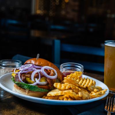 Brewhouse burger served with waffle fries and a beer on a wooden table.