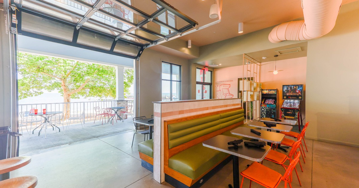 Interior, seating area with green bench seating, orange chairs, and arcade machines
