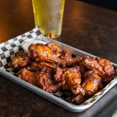 Sauced chicken wings served on checkered paper with a dipping sauce and beer.