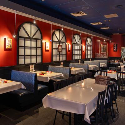 Booth seating along red wall with arched windows, tables and chairs.