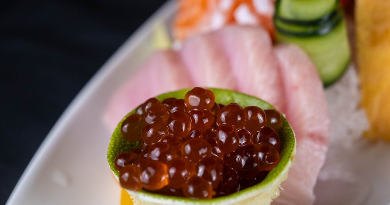 Salmon roe served in a lime cup with sliced sashimi in the background