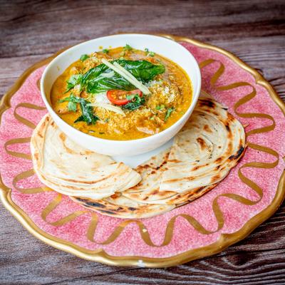 A bowl of coconut curried potatoes and chicken served with bread on a pink plate.
