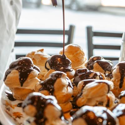 Chocolate sauce drizzling over a plate of profiteroles.