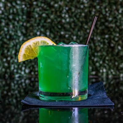 Liquid MJ cocktail drink, green colored, garnished with lemon wedge.