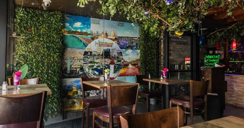 Interior of a restaurant with wooden tables and chairs, green foliage, a mural on the wall