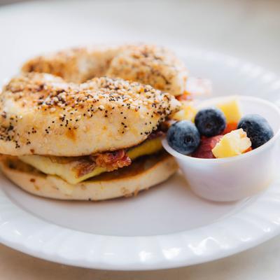 Breakfast bagel, with egg, cheese, and bacon, served with fresh fruit