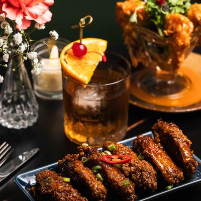 Plated chicken wings garnished with green onions and chilies, served with a cocktail.