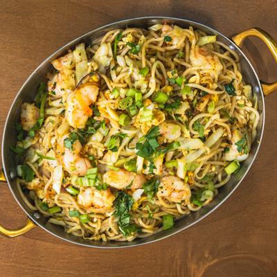 Shrimp stir-fried noodles topped with cabbage, scallions, and fresh herbs.