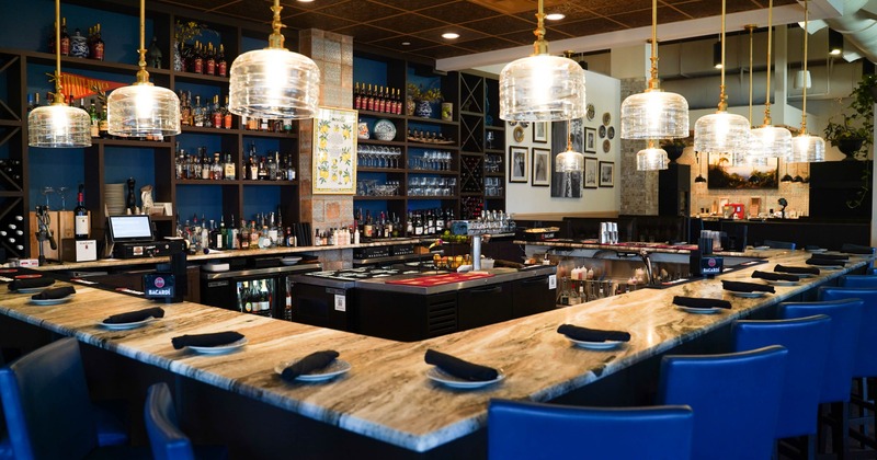 A modern bar with a marble countertop, blue bar stools and pendant lighting.
