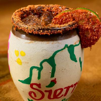 A cocktail in a colorful clay mug with a chili powder rim and lime.
