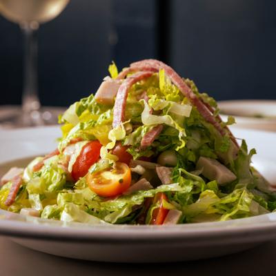 Chopped salad with lettuce, tomatoes, and salami strips.