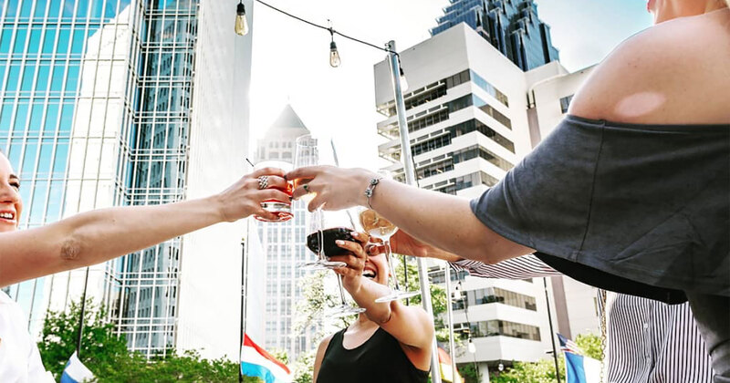 Outside in daylight, friends making a toast in the patio, tall buildings in the background