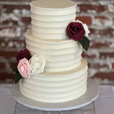 A tall three tiered wedding cake, decorated with garden roses