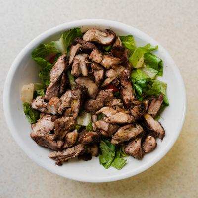A bowl of lettuce topped with pieces of grilled chicken.
